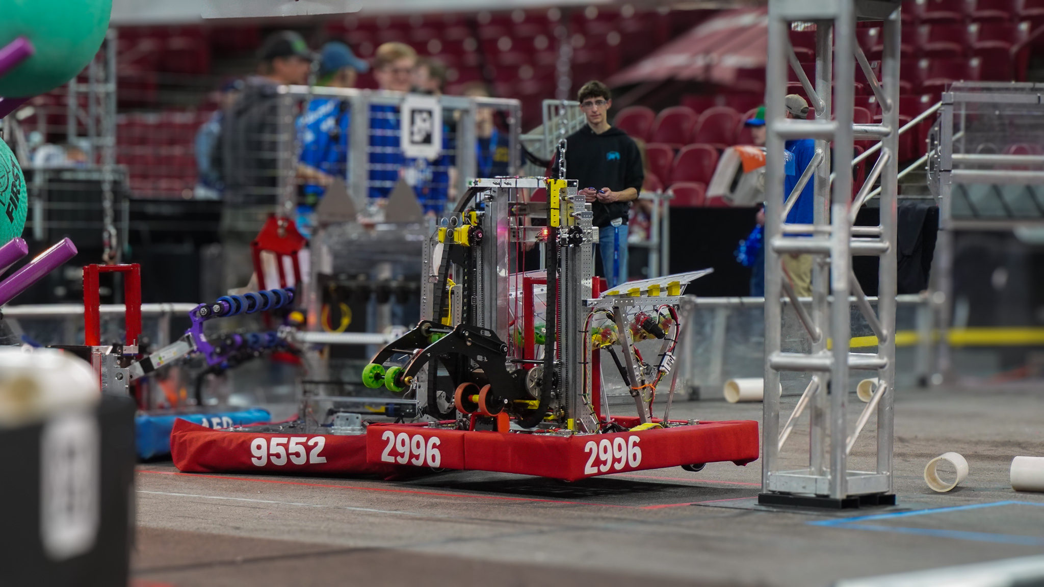 Robot 2996 competes on a field during a robotics match, surrounded by other bots and team members.