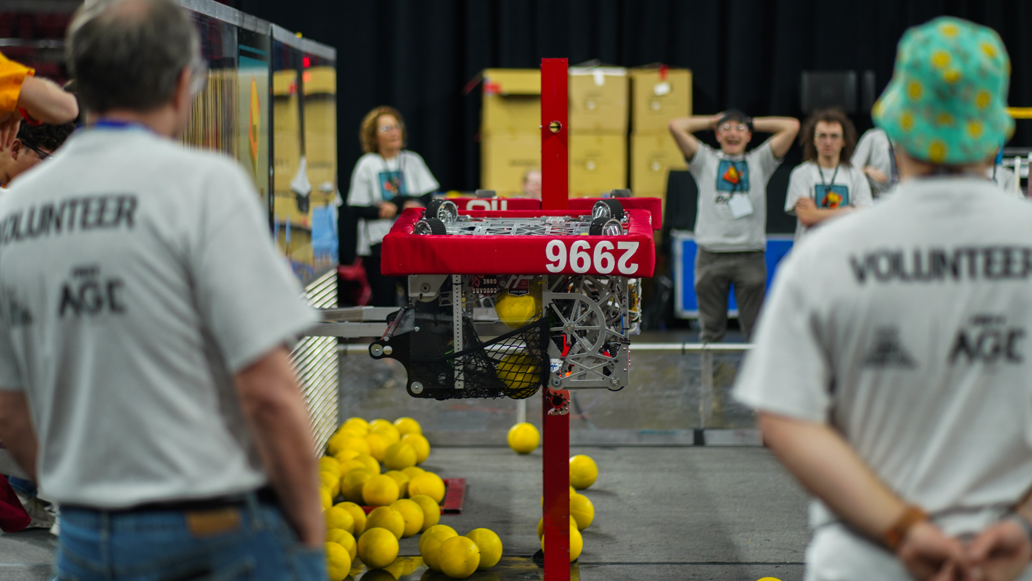Robot 2996 competes on a field during a robotics match, surrounded by other bots and team members.