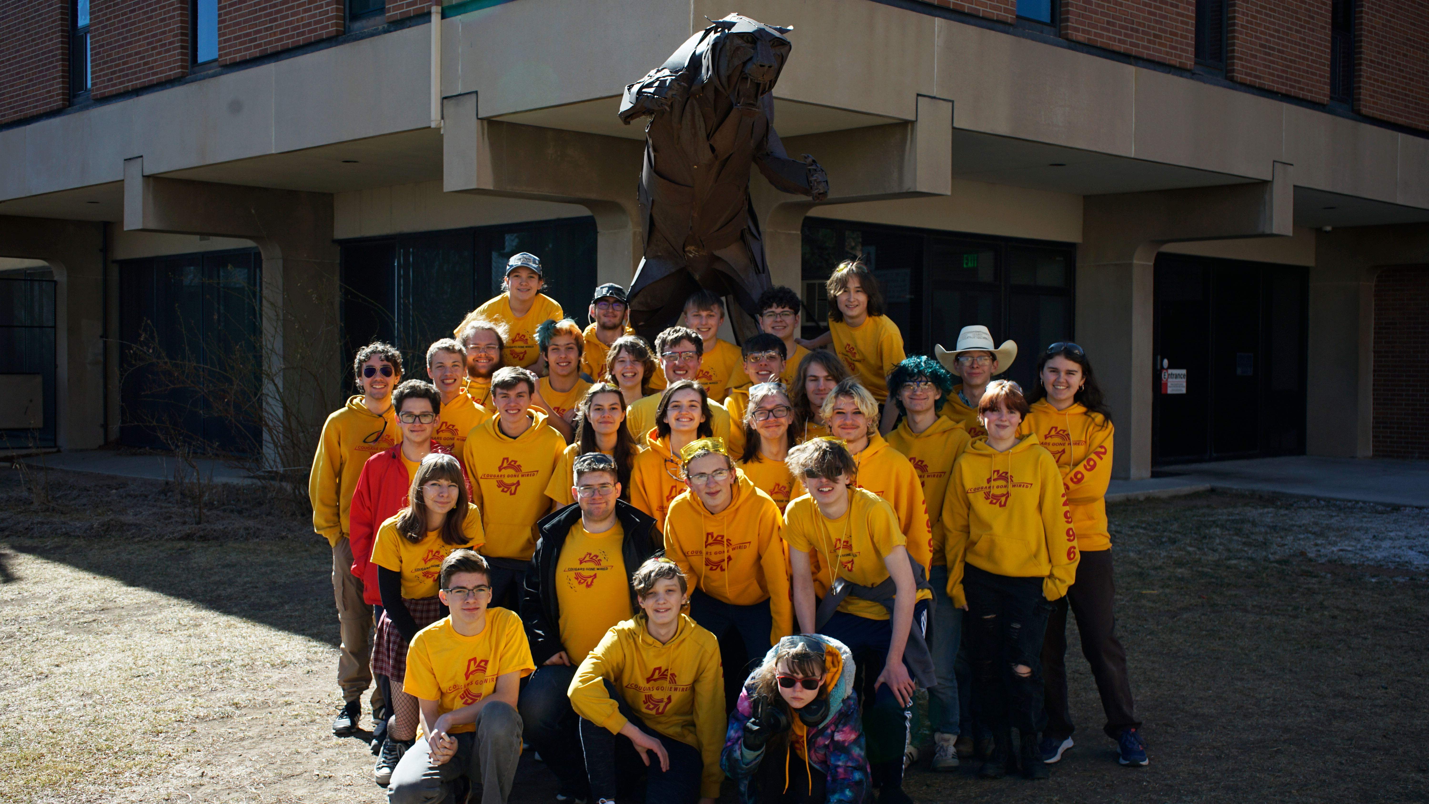 Team 2996 poses together on a robotics field, wearing yellow and red team shirts.